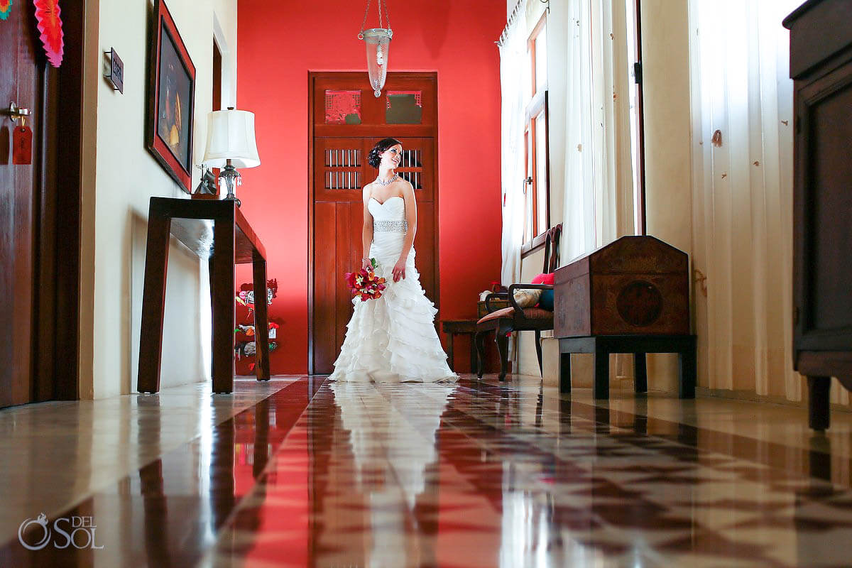 A bride holding her bouquet in a red-walled hacienda hallway