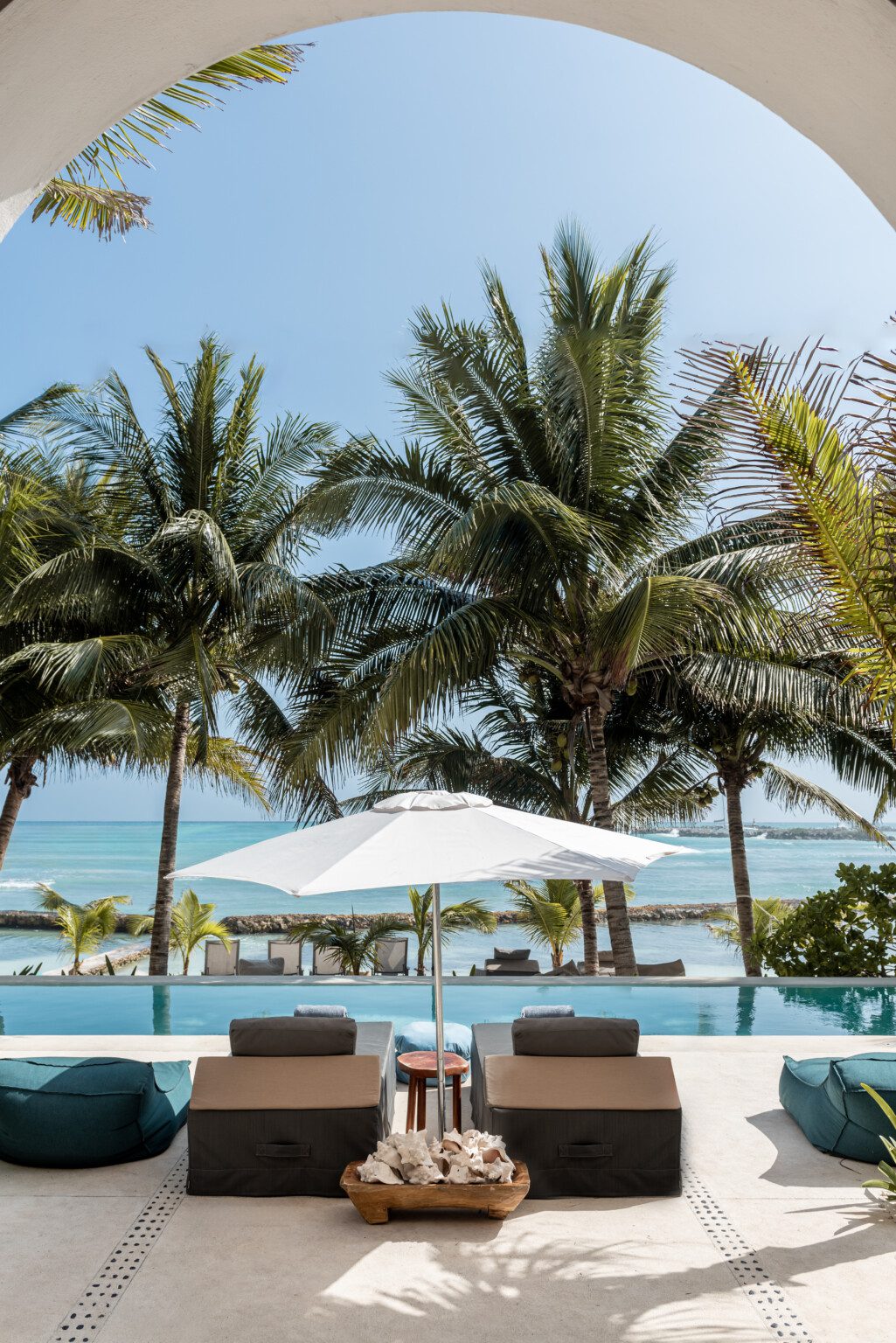 The pool and the Caribbean seen through an arch at Hacienda Del Mar, lounges under a white umbrella