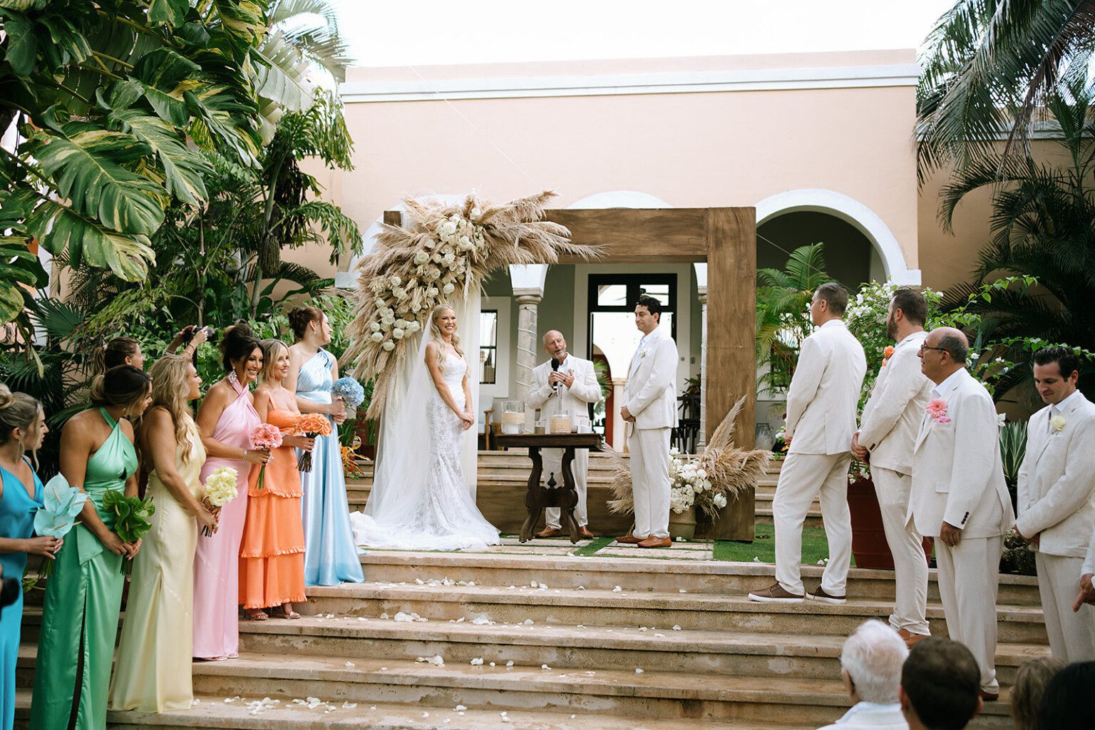 Guests in summer colours around a couple at a garden ceremony under a flowered arch