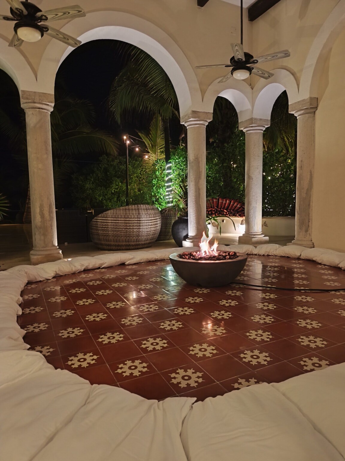 A fire bowl glowing in a cushioned lounge under lit stone arches at night