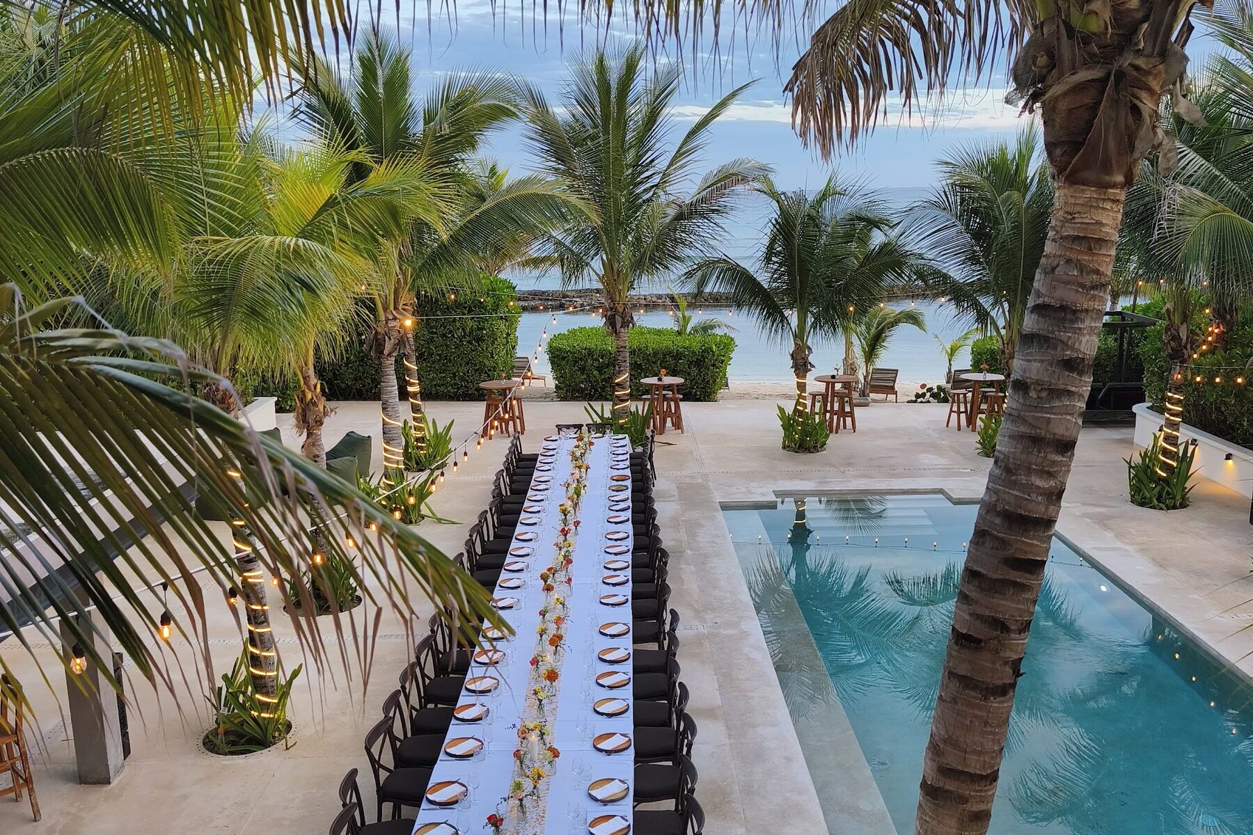 A long table set for a group beside the pool at Hacienda Jaguar, with palms, the beach and the sea beyond