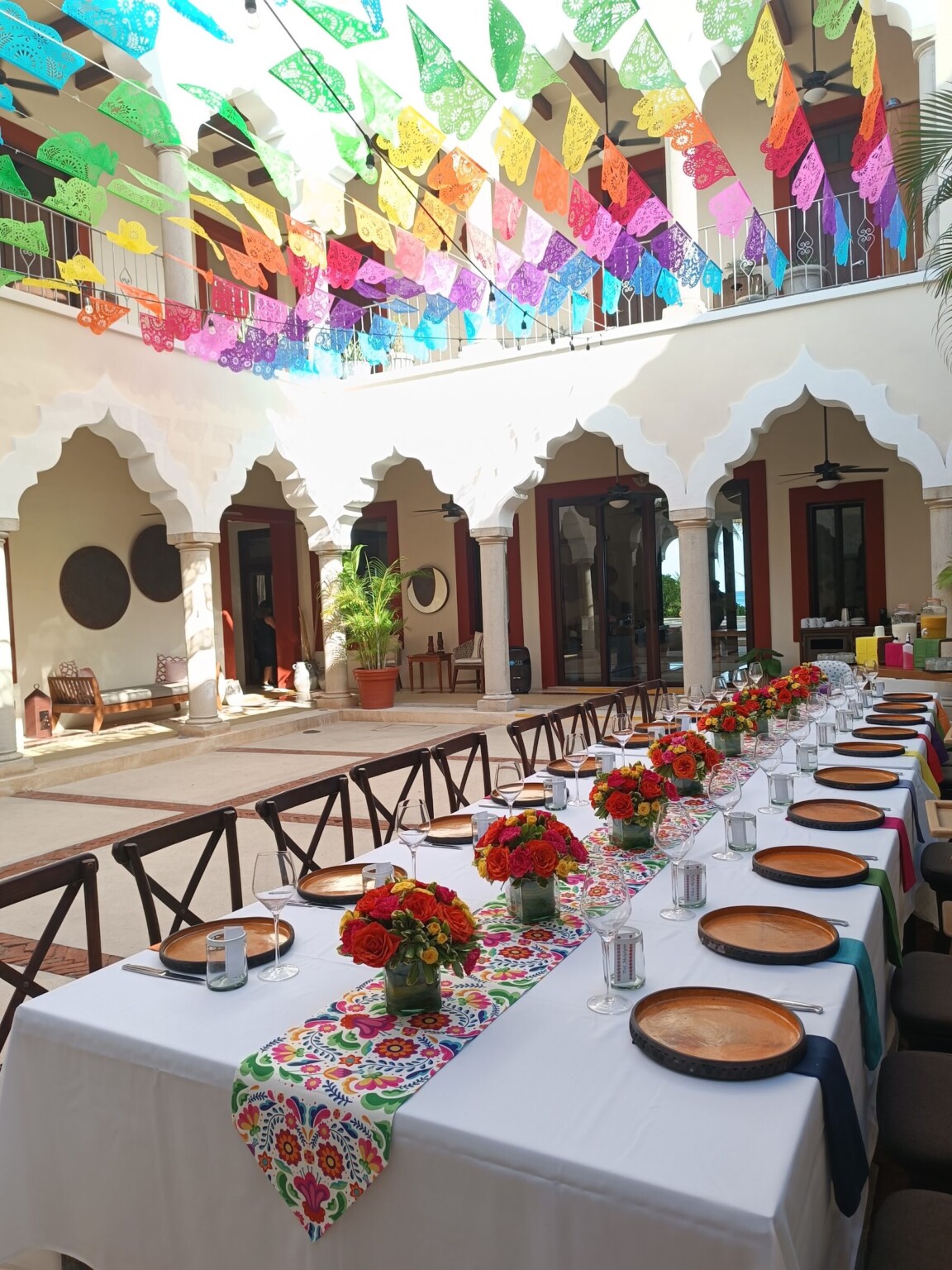 A long table under papel picado in a hacienda courtyard with scalloped arches