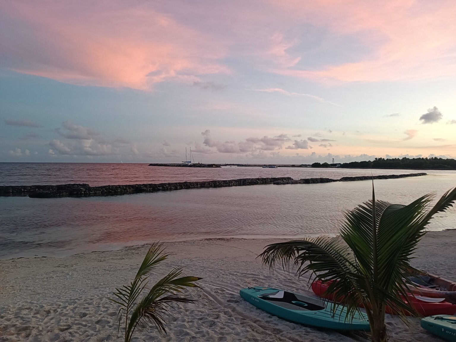 Kayaks on the sand in front of the haciendas at a pink sunset, the breakwater beyond