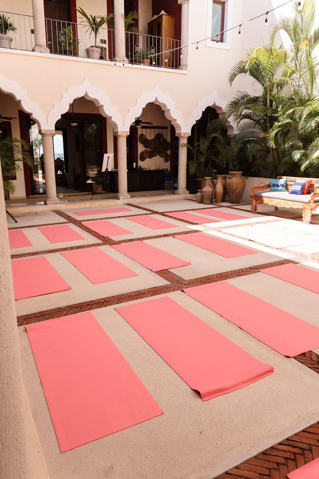 Pink yoga mats laid out in a hacienda courtyard with scalloped arches, morning light