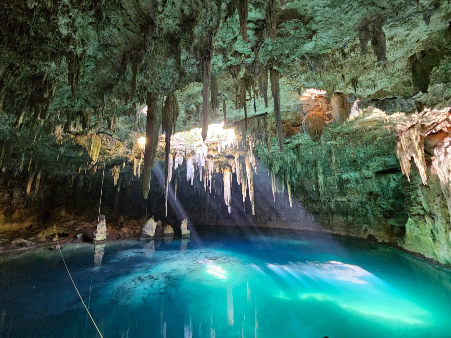 A cave cenote with blue water and hanging stalactites