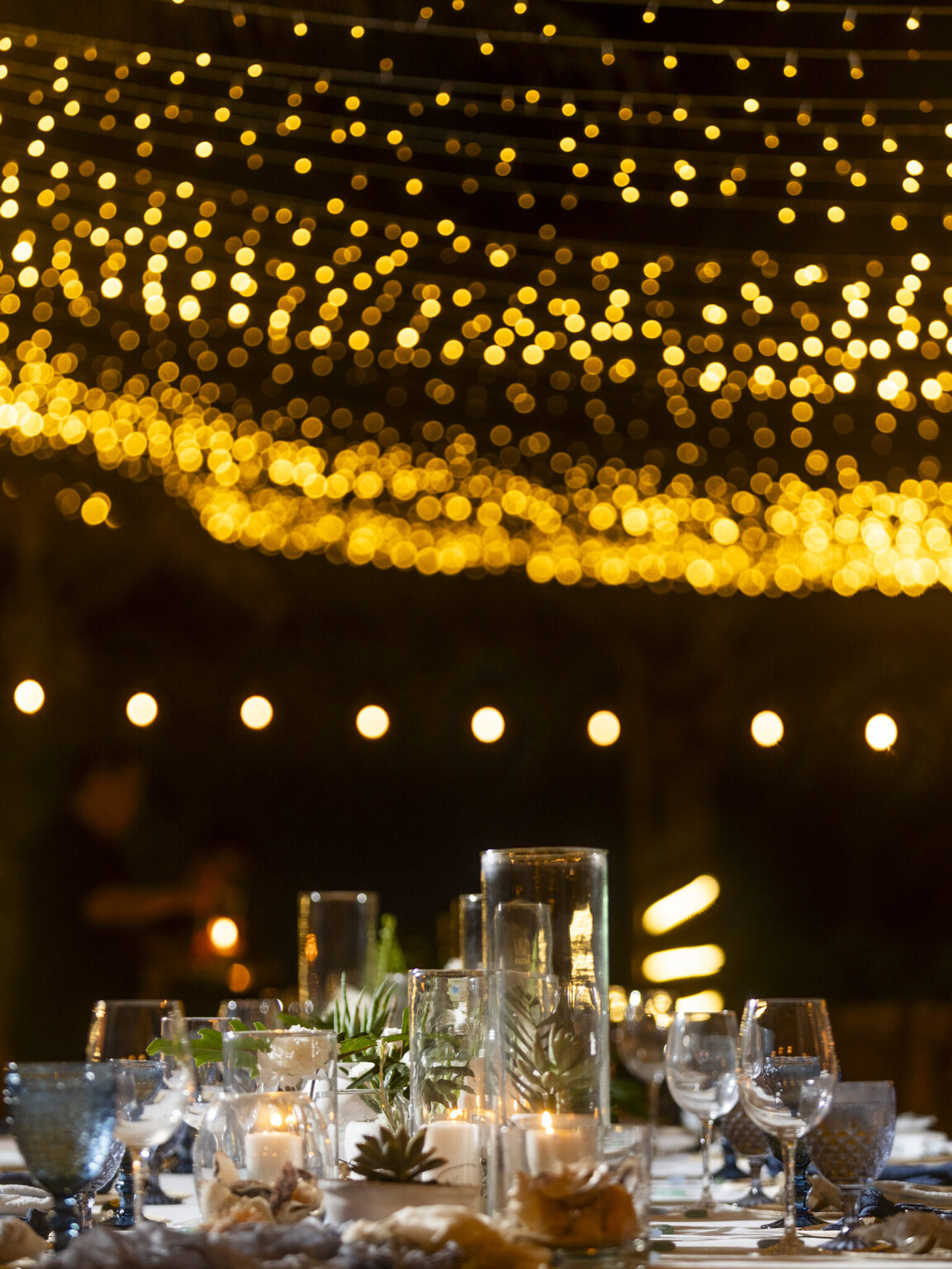 A candlelit table under a warm canopy of string lights at night