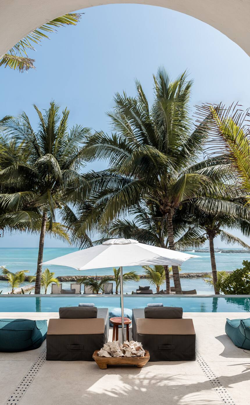 The pool and the Caribbean seen through an arch at Hacienda Del Mar, lounges under a white umbrella