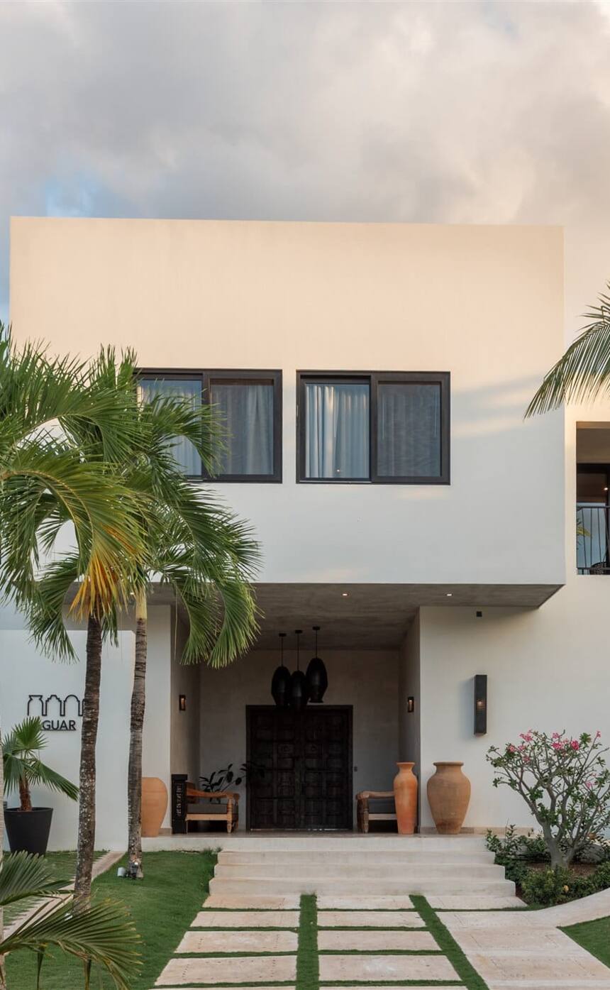 The white front of Hacienda Jaguar between palms, a stone path leading to its door