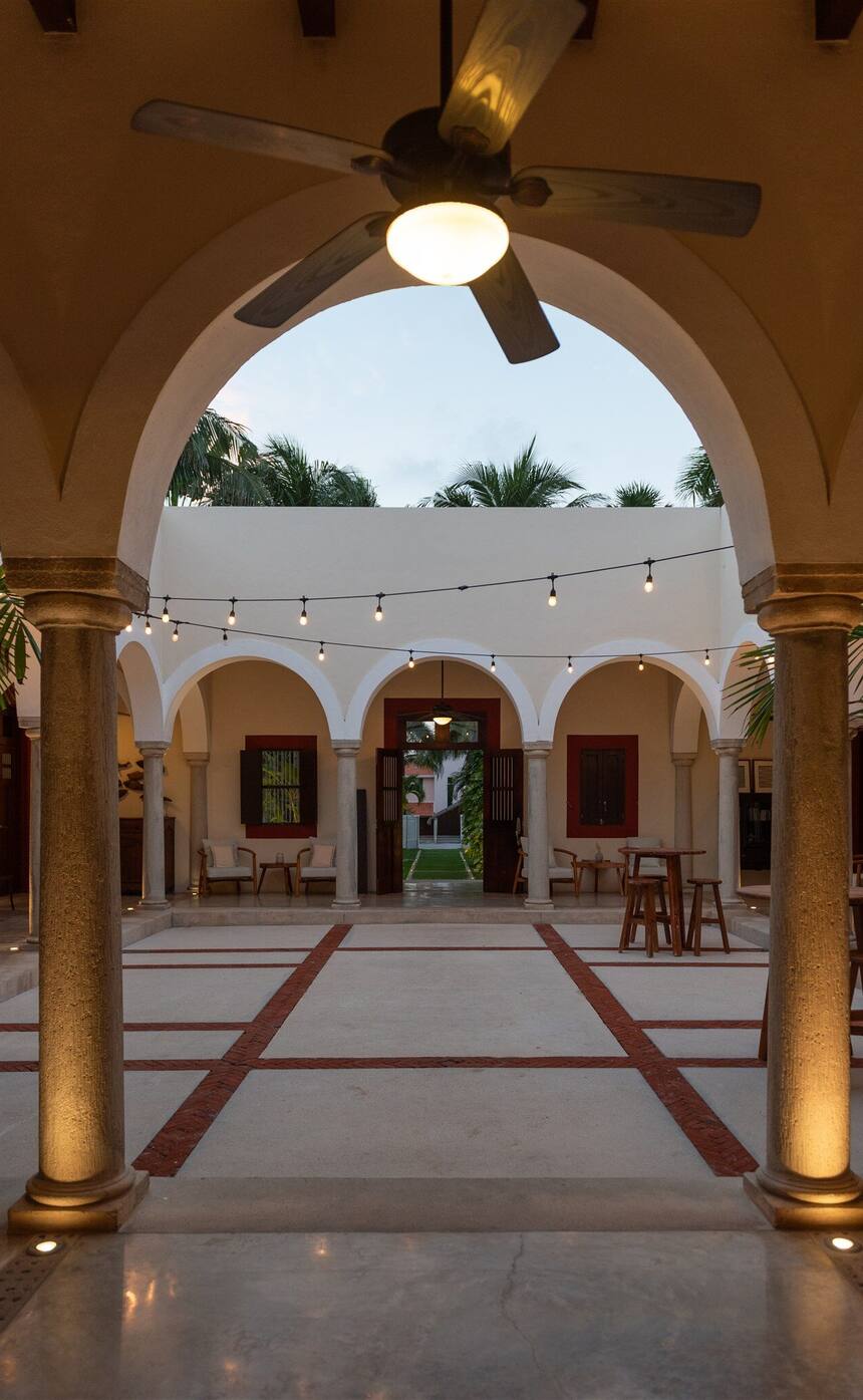 The courtyard of Hacienda Del Mar at dusk, seen through a lit arch, with string lights over the arcade