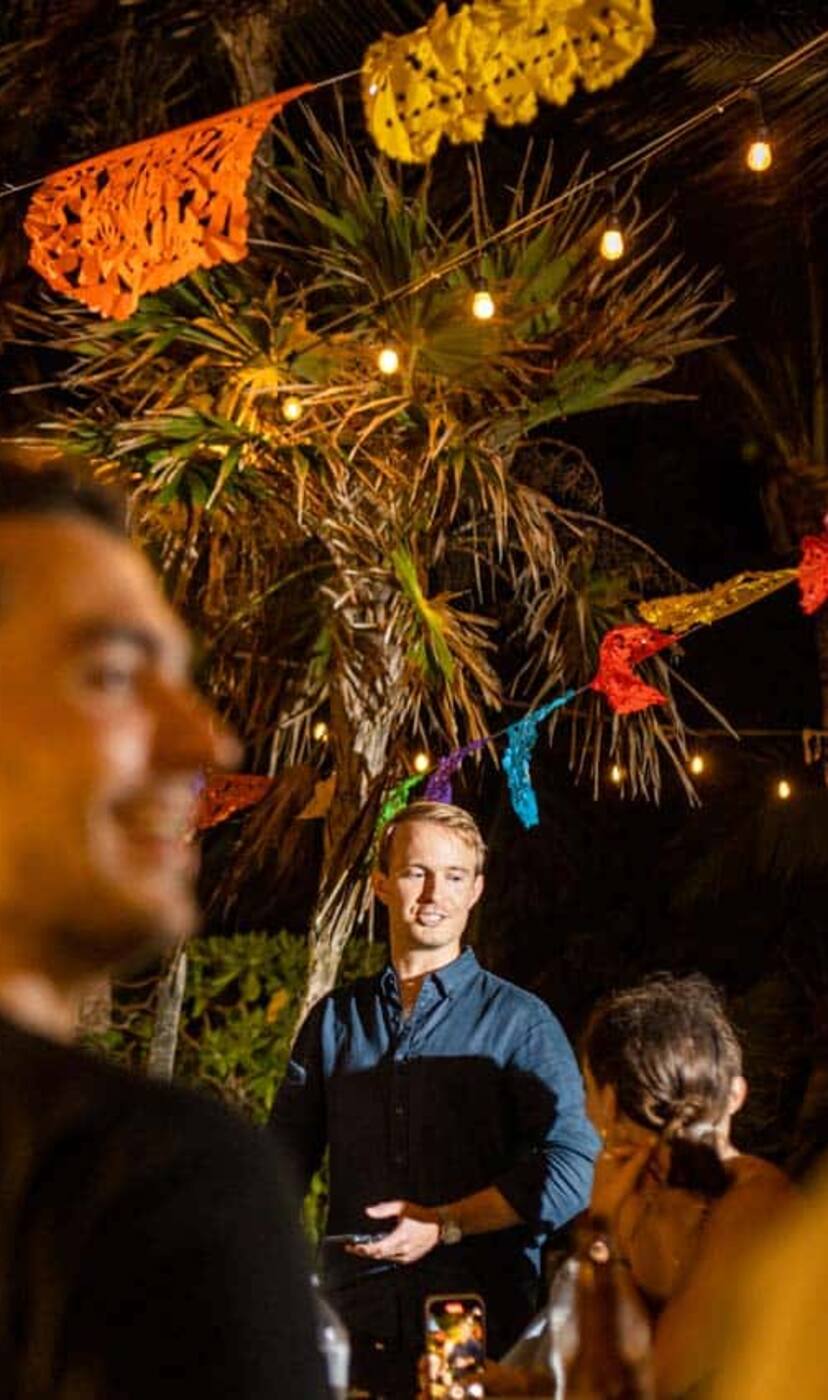Guests laughing under paper flags and string lights in a hacienda courtyard at night