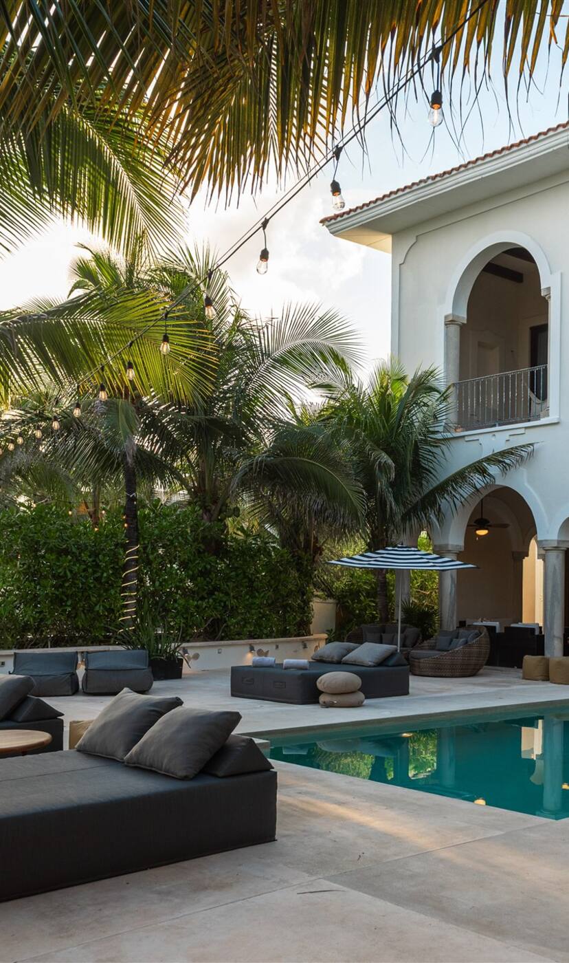 The white arcade and balconies of Hacienda Mágica over its pool, loungers under the palms